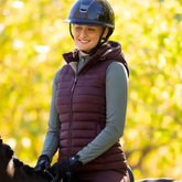 Person wearing a helmet and puffer gilet on a horse with a blurred autumn tree background
